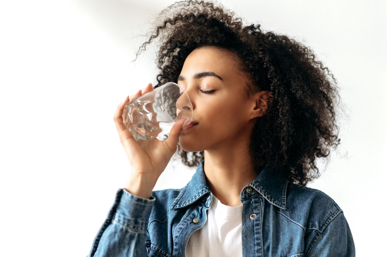 African american young woman drinks with pleasure a glass of pure water. Hydration for mental health